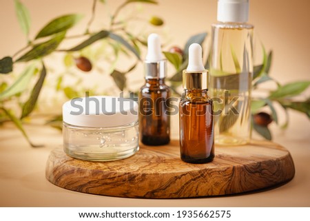 Olive based cosmetic serum, cream and water with sprig of olives on a pastel background