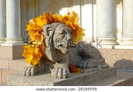 Statue of a lion wearing a crown of yellow autumn leaves on it