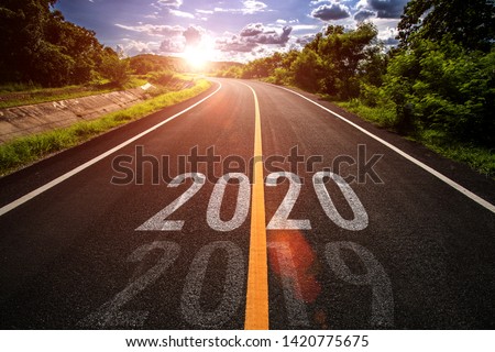 The word 2020 written on highway road in the middle of empty asphalt road at golden sunset and beautiful blue sky. Concept for new year 2020.