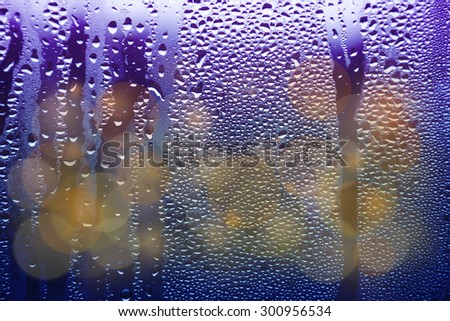 Drops of rain on window with bokeh lights background.
