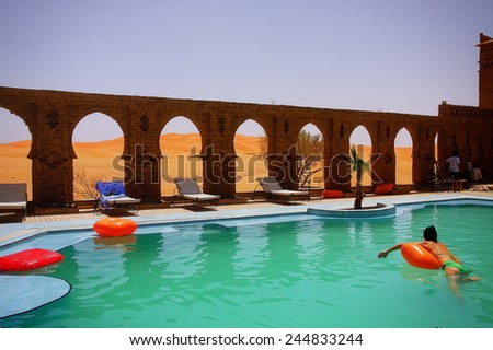 A beautiful moment of relaxation in a hotel swimming pool with ancient architecture amids moroccan desert dunes