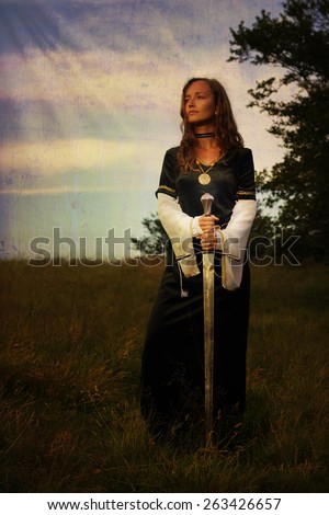mystical medieval woman  standing  with a sword on a wild meadow with enchanting evening light
