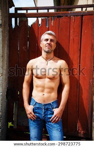 Sexy fashion portrait hot male model in stylish jeans with muscular body posing. Wolves tooth jewelery pendant.