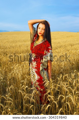 Young woman with ornamental dress standing on a wheat field with sunset. Natural background.