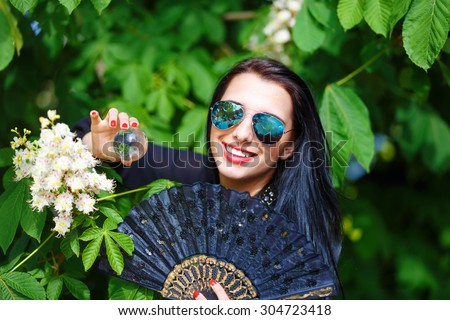 Young woman smelling a beautiful sakura blossom, purple flowers. Spring Magic, Magical Glass sphere in hand and beautiful ornamental fan. Flower background
