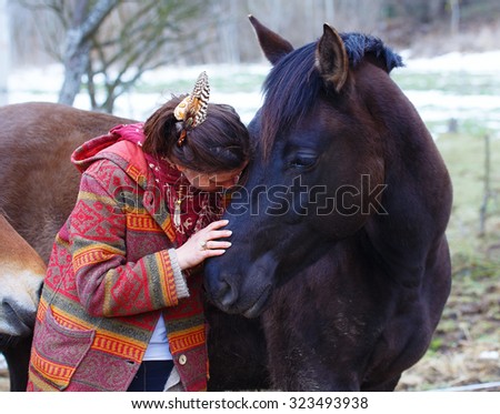 Portrait woman and horse in outdoor. Woman hugging a horse and has feather in her hair.