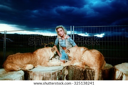 sexy blonde woman playing with lion cub on background with beautiful blue sky and storm clouds