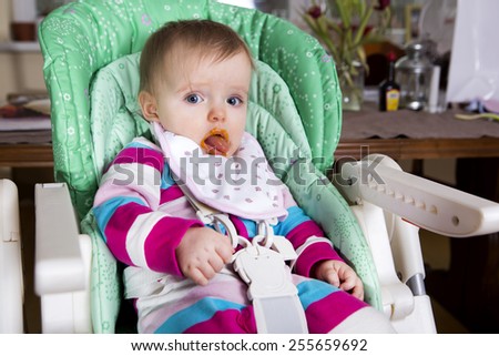 Naughty baby eating alone in the high chair. Dirty face