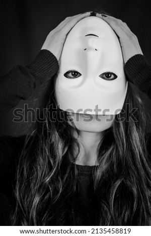 Being different even when wearing a mask - portrait of a young long-haired woman with a mask upside down and hands on her head - concept 商業照片 © 