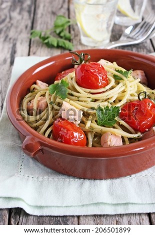 Servings of fresh spaghetti with green pesto, salmon and baked tomatoes.