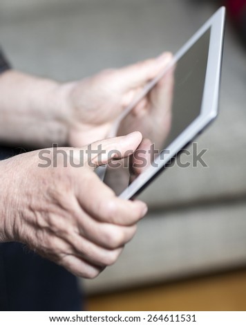 An elderly man browsing the internet with a tablet in a living room and sitting in a sofa.