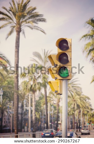 A traffic light showing green next to palm trees in the streets of Barcelona, Spain. Image has a vintage effect.