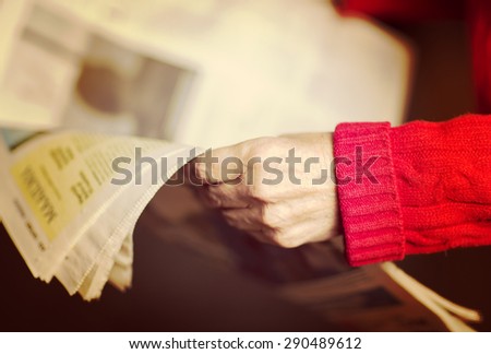 An elderly woman is reading a newspaper. Image has a vintage effect.