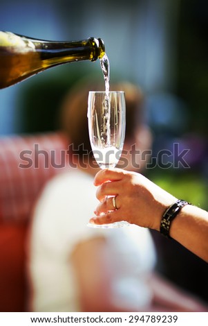 An image of pouring champagne to a glass outdoor and in the summer time. Image has a vintage effect applied.