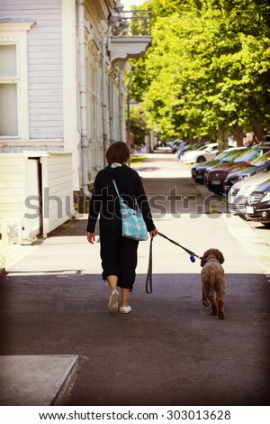 A woman is walking the dog in the streets. The dog is lagotto romagnolo also known as Italian waterdog. Image has a vintage effect applied.