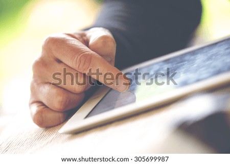 An older man is browsing the internet with a white tablet outdoor. Image has a vintage effect applied.