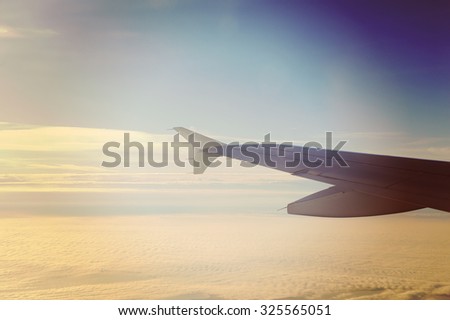 An airplane wing against the sky and clouds up in the air. Image has a strong vintage effect applied.