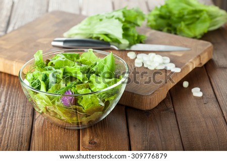 Bowl of seasoning salad over chopping board with sliced onions and lettuce leaves background on wooden table