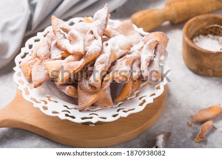 Italian Frappe or chiacchiere (hvorost) - typical Italian carnival fritters dusted with powdered sugar on concrete  table.