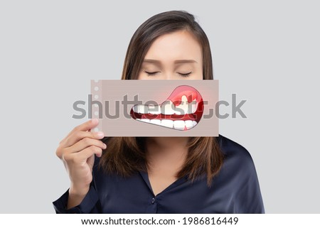 Asian woman in the dark blue shirt holding a paper with the broken tooth cartoon picture of his mouth against the gray background, Decayed tooth, The concept with healthcare gums and teeth Foto stock © 