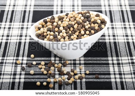 French Mignonette Pepper - White and black peppercorns in a white porcelain bowl on black and white white fabric.