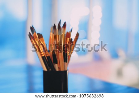 Assorted dirty painting brushes in glass flask. blue background