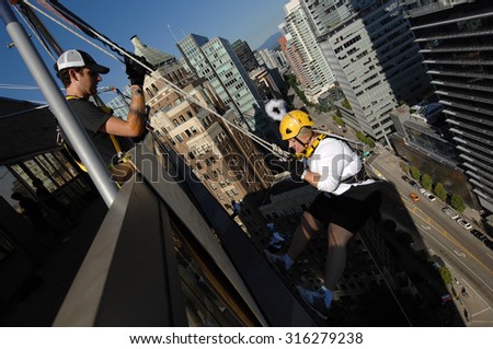 VANCOUVER, CANADA - SEPTEMBER 10, 2014: A woman climbs down office building during Easter Seals Drop Zone fundraiser to benefit children with disabilities in Vancouver, Canada, on September 10, 2014.