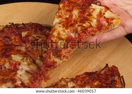 Hand taking a slice of freshly baked ham and pineapple pizza cut into slices