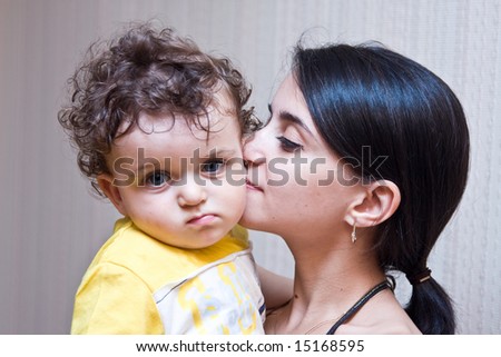 Mum kisses the son on a cheek, the boy looks in lens