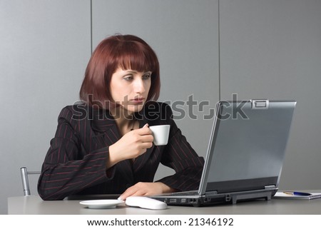Beautiful businesswoman behind a desktop and a laptop with a coffee cup in a hand