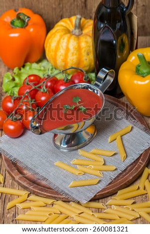 Tomato sauce in a white sauce boat with fresh ingredients and pasta