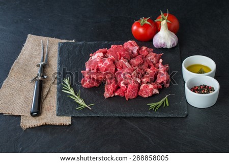 Raw beef cubes with rosemary and beefsteak spices on black background