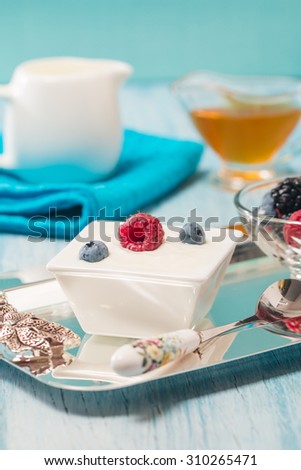 Bowl of fresh mixed berries and yogurt with farm fresh raspberries, blackberries and blueberries on a blue wooden table