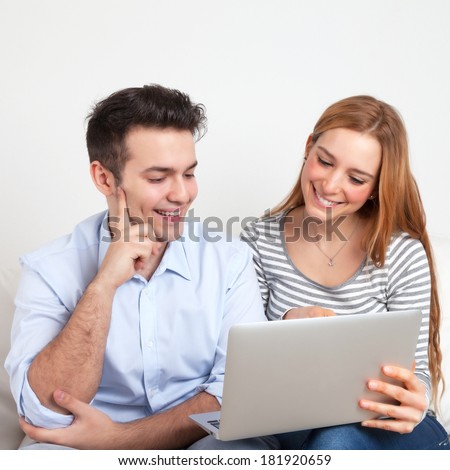 Laughing young couple on a sofa looking on a notebook screen