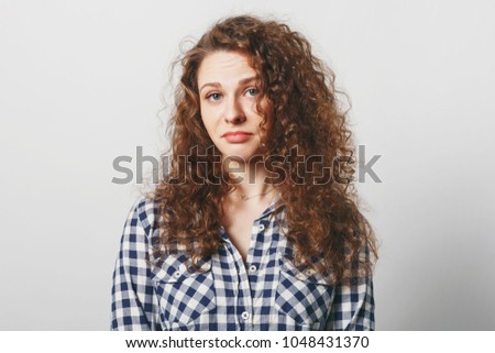 Unhappy beautiful woman with displeased look has attractive look and curly hair, looks at camera with bewilderment, being puzzled as makes serious decision, isolated over white studio background Foto d'archivio © 