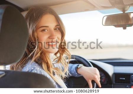 Close up portrait of pleasant looking female with glad positive expression, being satisfied with unforgettable journey by car, sits on driver`s seat, enjoys music. People, driving, transport concept Foto stock © 