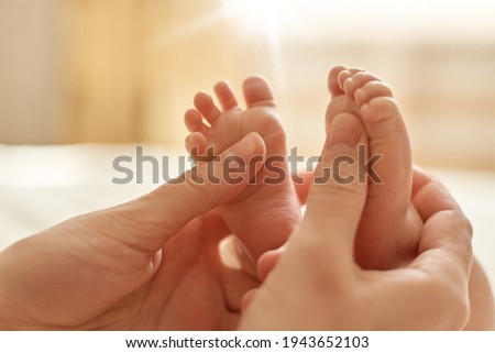 Mum making baby massage, mother massaging infant bare foot, preventive massage for newborn, mommy stroking the baby's feet with both hands on light background.