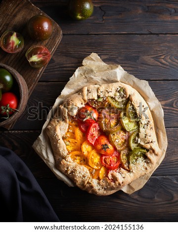 Pie with different varieties of tomatoes. Red tomatoes, yellow tomatoes, green tomatoes. Gradient on baking. Tomato biscuit on a brown wooden table. A delicious aperitif. Mediterranean cuisine. Vegan