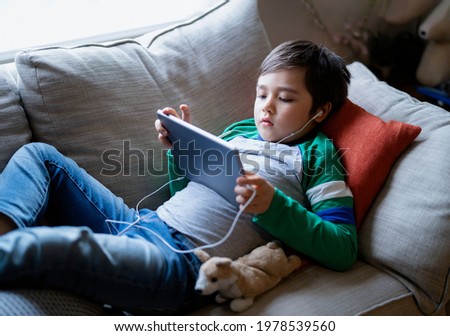 Similar – Image, Stock Photo Child sitting with headphones on a sofa with tablet computer looking frontally at night