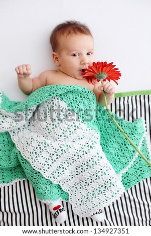 Small boy lies under a blanket with flower Gerbera Daisy. Age one months.
