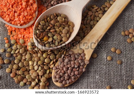 Green and red lentils in wooden spoons on sackcloth