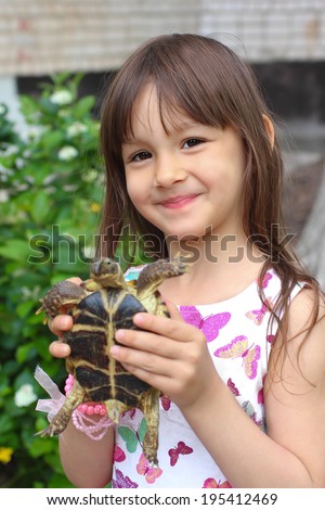 Smiling little girl holding a russian tortoise. Loving nature concept
