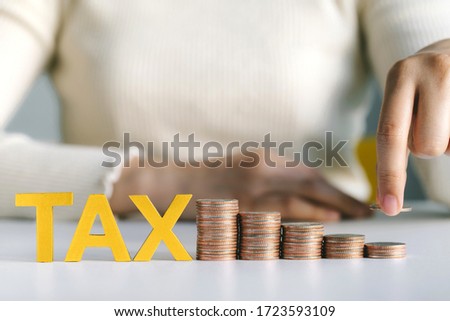 Close-up Of Hand holding coin putting on  stacked Coins and word tax on white table. Income Tax Raise Concept Photo stock © 
