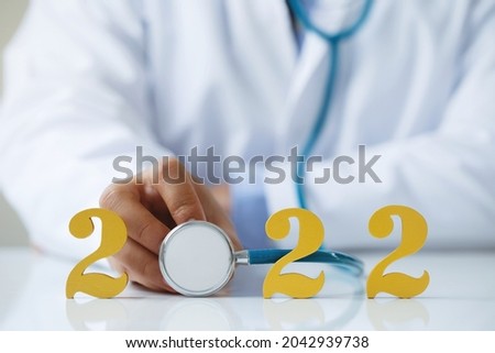 Doctor holding stethoscope near gold wooden number 2022 on desk. Idea for new trend in medicine treatment and diagnosis.Happy New Year for healthcare and medical concepts.