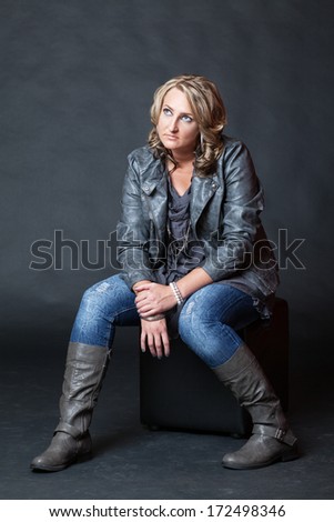 Young blonde woman wearing jeans and boots sitting on cube in studio