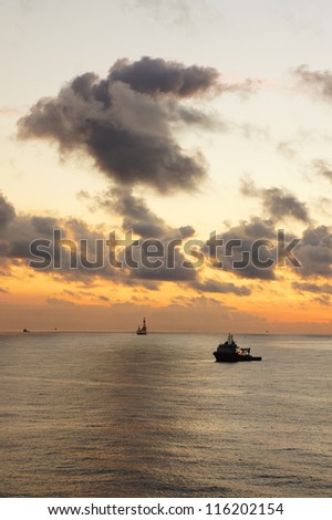 Supply boat and offshore drilling rig in the middle of the ocean at twilight time