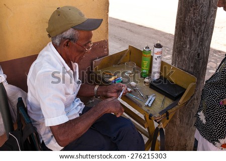 Trinidad, Cuba - 22 January, 2015: a old man works recharging lighters with gas on a sidewalk.