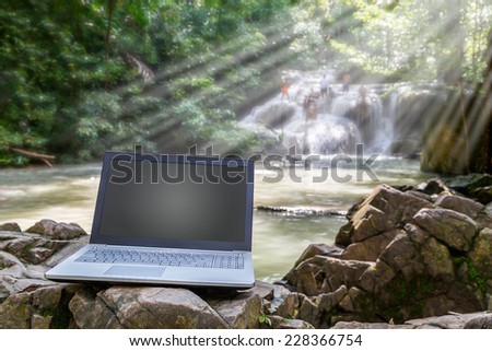 Notebook computer put on the rock in the front of waterfall in National Park, Thailand