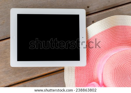 Tablet white frame and black screen  with  Beautiful woman\'s hat on wooden floor in  summer theme