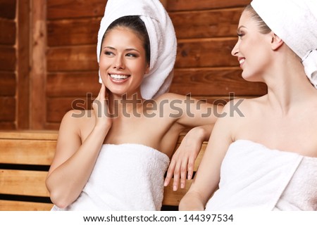 Two beautiful laughing females sitting and talking in sauna